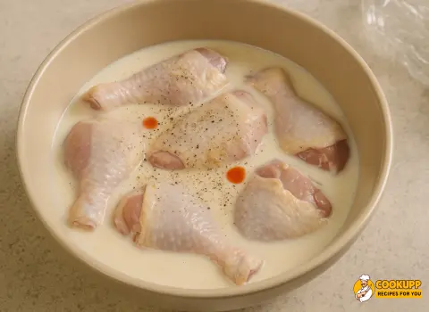 Chicken pieces soaking in a buttermilk, salt, pepper, and hot sauce marinade in a glass bowl