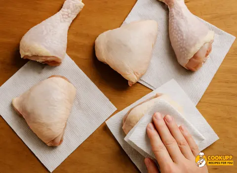 Raw chicken pieces being patted dry with paper towels before marinating